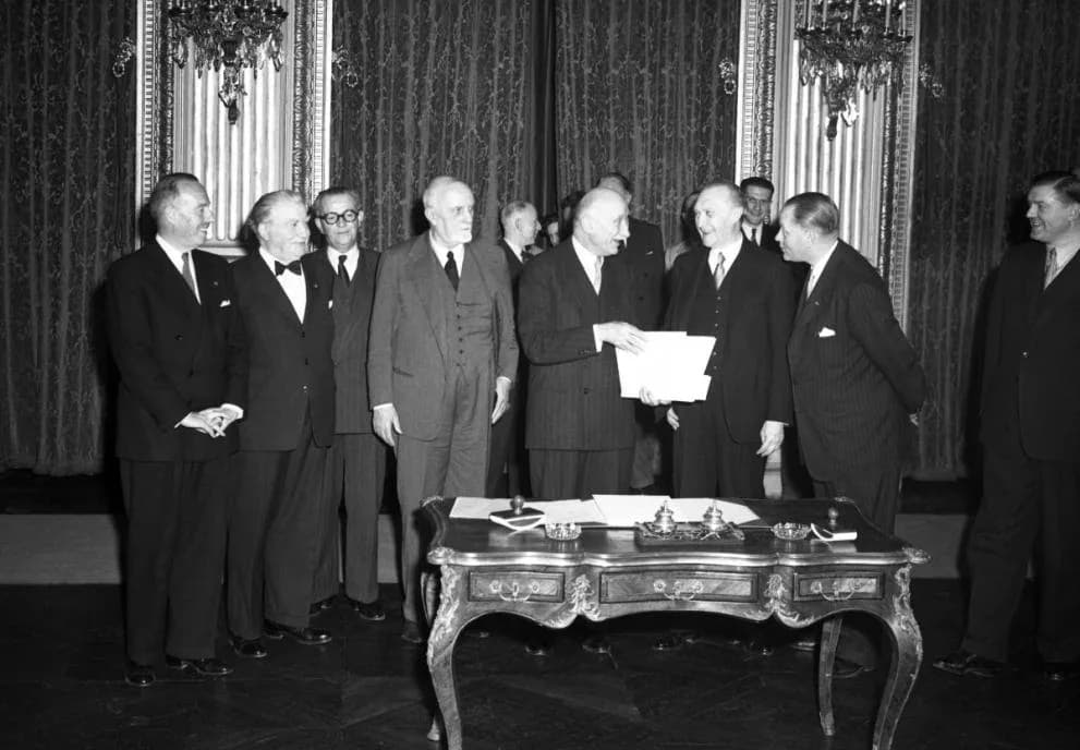 Black-and-white photograph of European statesmen gathered around a desk at a treaty signing in the early 1950s.