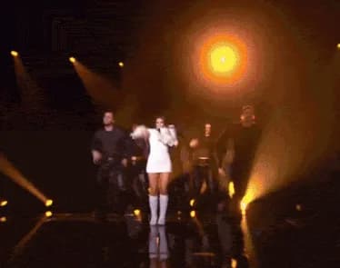 GIF of a Eurovision Song Contest performance, the singer centre stage in a spotlight with dancers behind her.